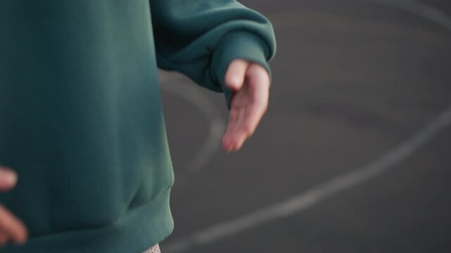 Close-up of person in green hoodie flapping hand over markings on ground, preparing for volleyball serve with focus on hand movement and training markings on outdoor sports court
