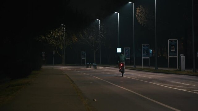 cyclist rides alone under dim streetlights near Jarun Lake, Zagreb, evoking solitude