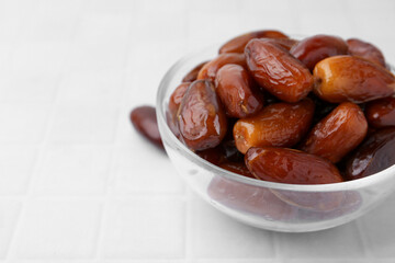 Tasty dried dates in glass bowl on white table, closeup. Space for text