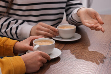 Coffee break. Women with cups of hot drinks at wooden table indoors, closeup