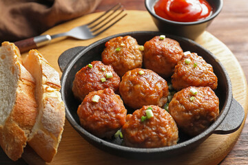 Tasty meatballs with green onion in baking dish served on wooden table