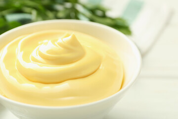 Delicious mayonnaise sauce in bowl and parsley on white wooden table, closeup