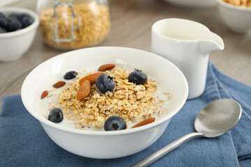 Tasty oatmeal with milk, blueberries and almonds in bowl served on table, closeup