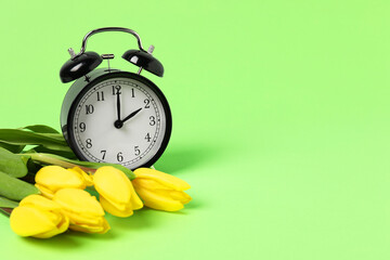 Spring time. Alarm clock and beautiful tulips on green background, space for text