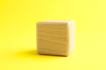 One blank wooden cube on yellow background, closeup