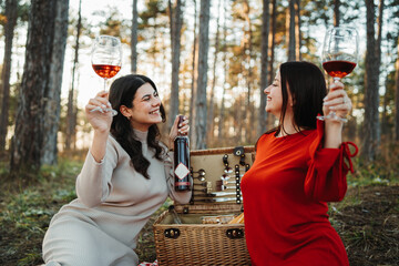 Two young caucasian woman have picnic drink wine in the forest