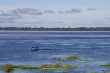Fototapeta premium Un bote rústico, con personas no identificadas navegando sobre las aguas del rio Amazonas cerca a la ciudad de Iquitos en la amazonia peruana