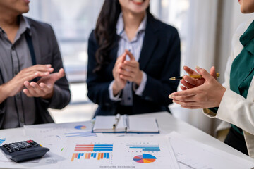 Three people are standing around a table with papers and a pen