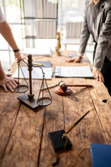 A scale sits on a wooden table with a judge's gavel and a pen