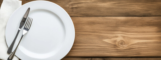 Photo of a white plate, fork, and knife on an empty wooden tabletop
