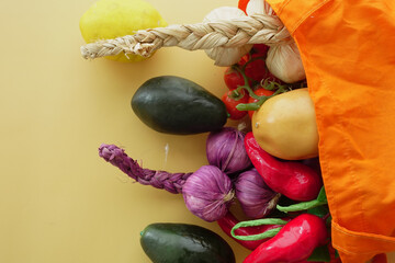 Fresh vegetables spilling from a reusable bag on a yellow background