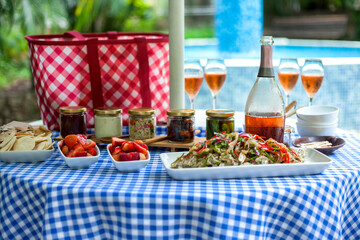 Delicious food and drinks laid out on checkered tablecloth for poolside summer picnic