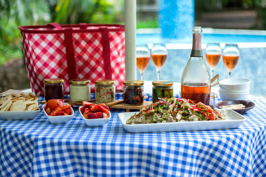 Delicious food and drinks laid out on checkered tablecloth for poolside summer picnic