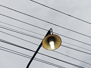 Single streetlight illuminated against cloudy sky with power lines lamp pole grey urban wires metal