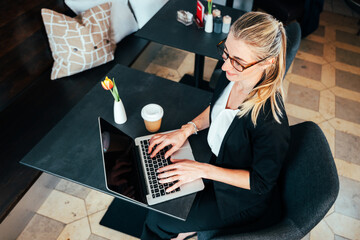 A blonde businesswoman sitting in a café, working on her laptop, writing an article as a blogger...