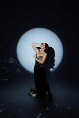 A woman in a metallic dress poses under a dramatic spotlight. Her confident stance and artistic...
