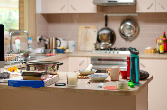 A cluttered kitchen counter in a residential house with various household items scattered across it. An untidy domestic cooking space at home in need of cleaning.
