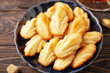 Madeleine cakes in plate and a cup of tea on wooden background
