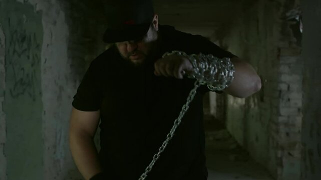 Muscular strongman wrapping heavy metal chain around arm, embodying intense strength performance within grungy abandoned industrial corridor under dramatic lighting