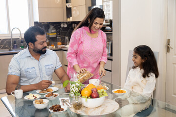 Naklejka premium indian family having breakfast together at home. mother making cereal with milk in bowl for her daughter.