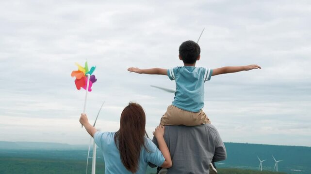 Concept of progressive happy family enjoying their time at the wind turbine farm. Electric generator from wind by wind turbine generator on the country side with hill and mountain on the horizon.
