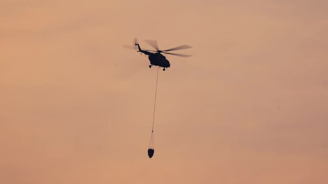 Fire fighting helicopter carry water bucket to put out a forest fire.
