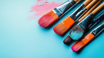 Fototapeta premium Colorful Paintbrushes on a Pastel Blue Background with Pink Paint Stroke