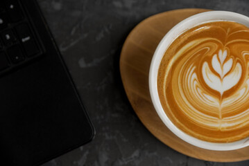 A laptop on a black table next to a white cup of coffee on a white background.