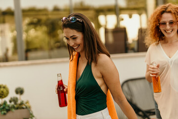 Two happy women holding drinks and smiling at a rooftop party