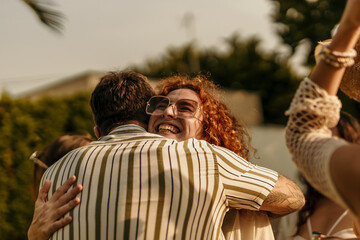 Group of friends laughing and hugging at a summer party, drinking bottled beverages