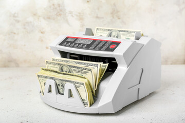 Modern cash counting machine with dollar banknotes on light background