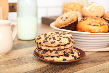Bottle with milk, cookies and cupcakes on wooden table in kitchen