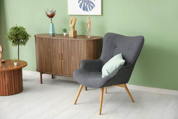 Dark grey armchair with pillow, dresser and coffee table near green wall