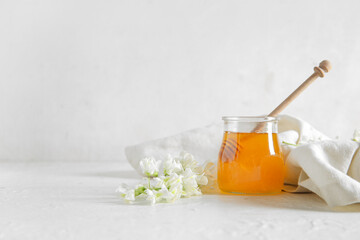 Jar of honey with flowers of acacia and dipper on light background