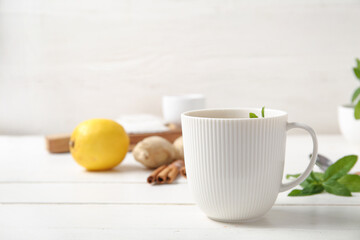 Cup of fresh mint tea with lemon, ginger root and cinnamon on white wooden table