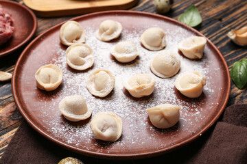 Plate with uncooked dumplings on wooden background