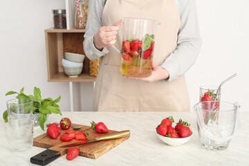 Woman holding jug of lemonade with strawberry and mint in kitchen