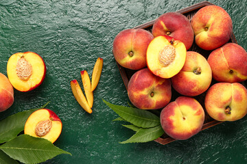 Tray with sweet peaches and leaves on green background