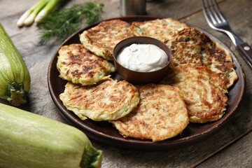 Plate of tasty zucchini fritters with sour cream on wooden background
