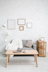 Interior of stylish living room with sofa and blank frames on white brick wall