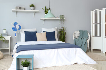 Interior of light bedroom with cozy bed and floor fan