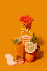 Glass of tasty citrus cocktail with fruits and flower on orange background