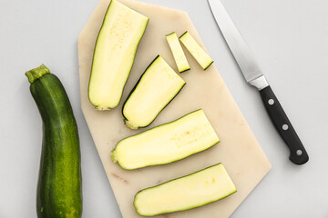 Board with slices of fresh green zucchini on white background