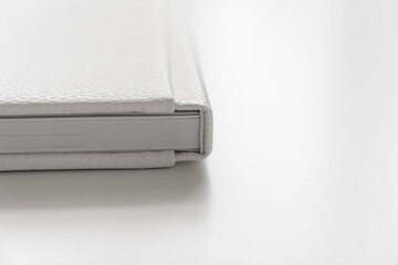 corner of book in white leather cover on white table. binding for photo album