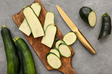Wooden board with slices of fresh green zucchini on grey background