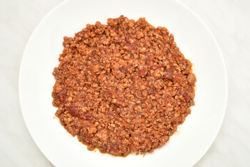 Stewed mixed pork and beef minced meat with peeled and chopped tomatoes in tomato juice on the white plate on the light gray marble table texture. Top view.