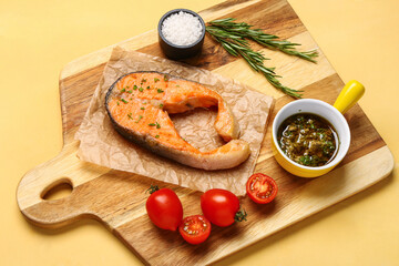 Wooden board of tasty salmon steak with tomatoes and sauce on yellow background