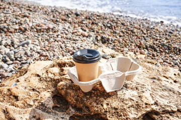 Holder with takeaway cup of hot coffee on beach