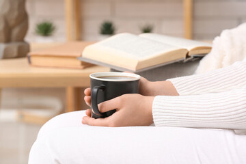 Woman holding cup of tasty coffee at home, closeup