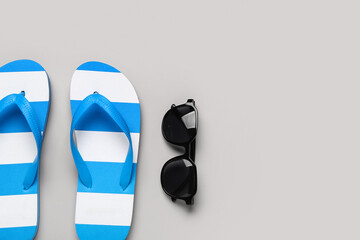 Female stylish flip flops with sunglasses on grey background